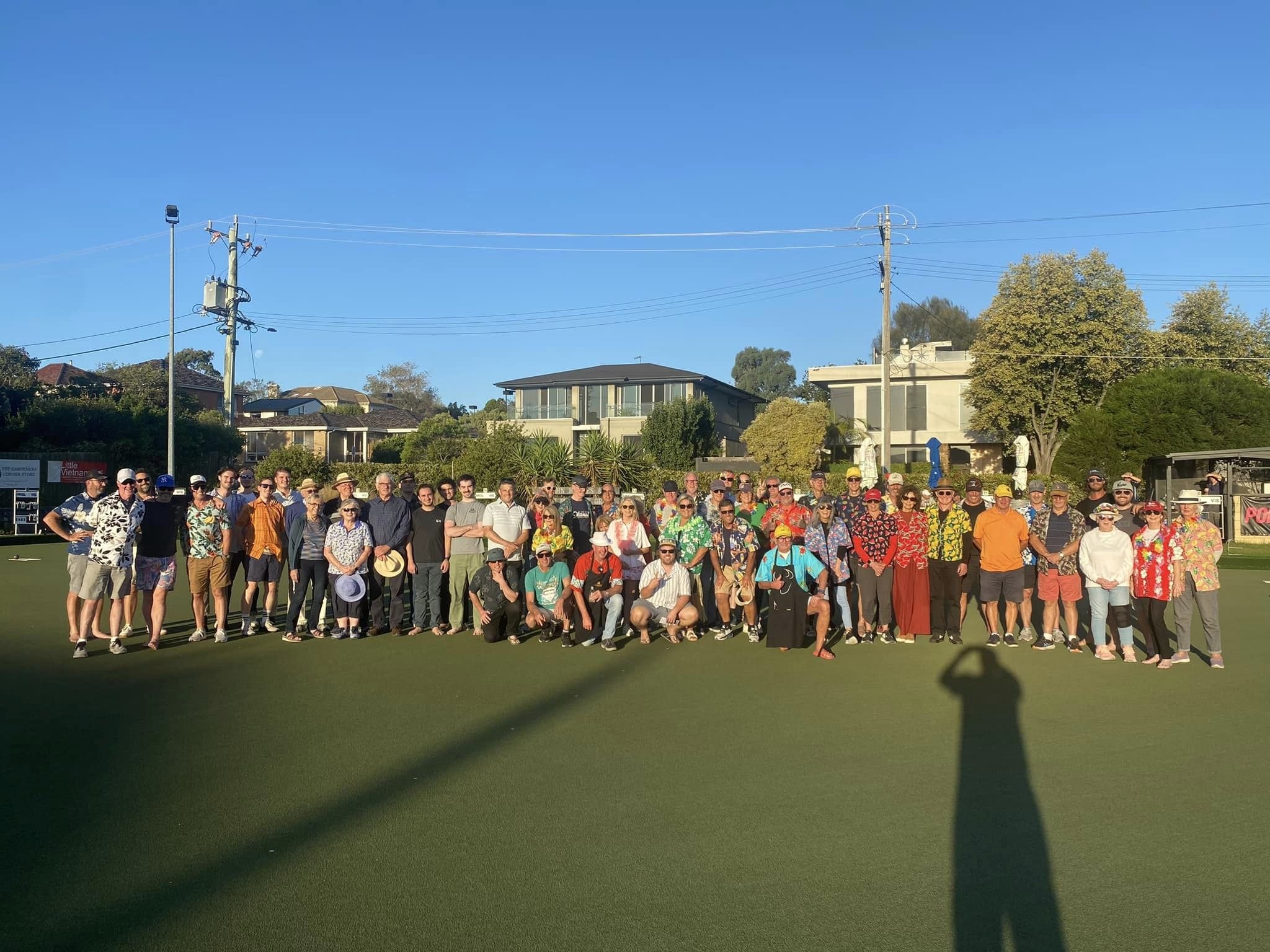 A big barefoot bowls crowd in Hawaiian shirts on the green