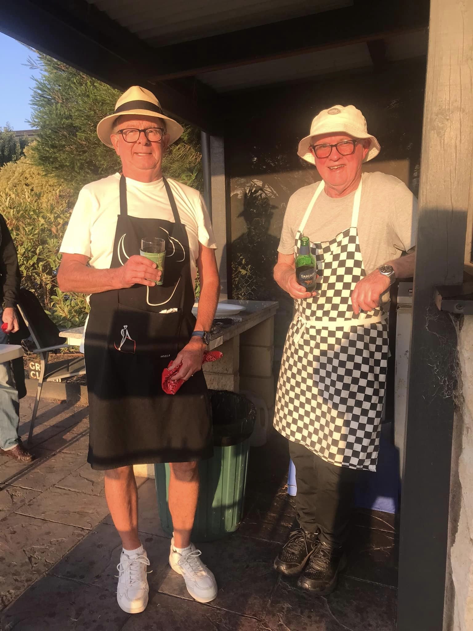 Two members in aprons and hats running the barbecue at the club